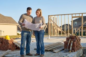 Un couple de particuliers consulte des plans architecturaux sur un chantier de construction de maison individuelle